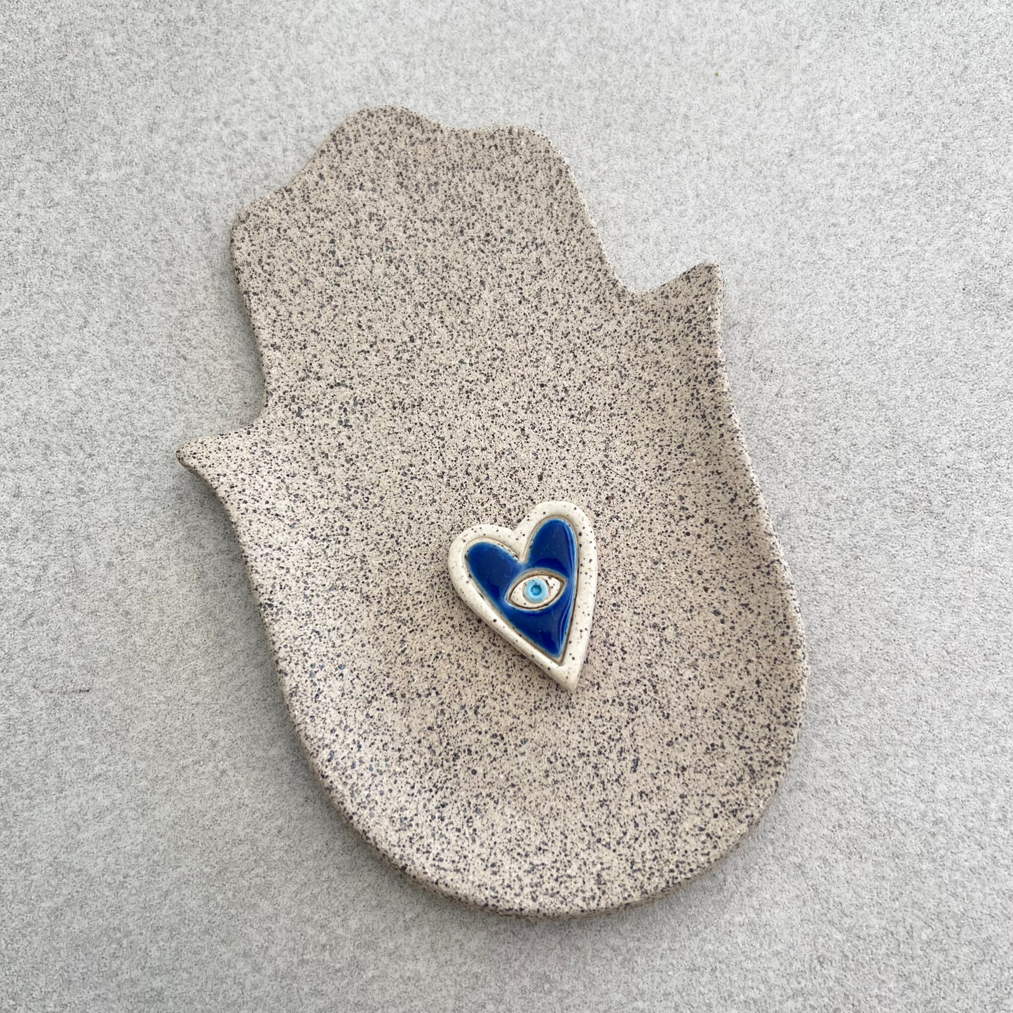 A ceramic Hamsa hand-shaped dish with a blue evil eye in the center