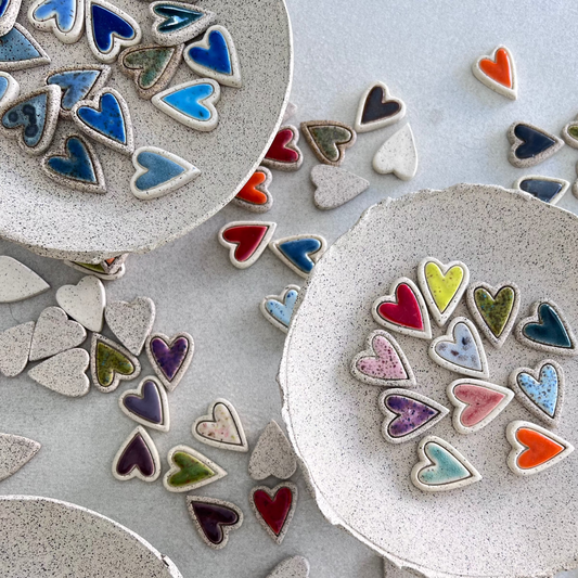 A collection of colorful ceramic hearts in various colors displayed on a bare clay bowl